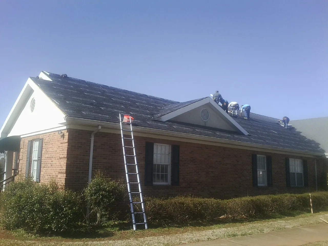 Crew tearing shingles off a brick ranch roof with a ladder set — Emergency Roof Repair work by our crew in Toughkenamon