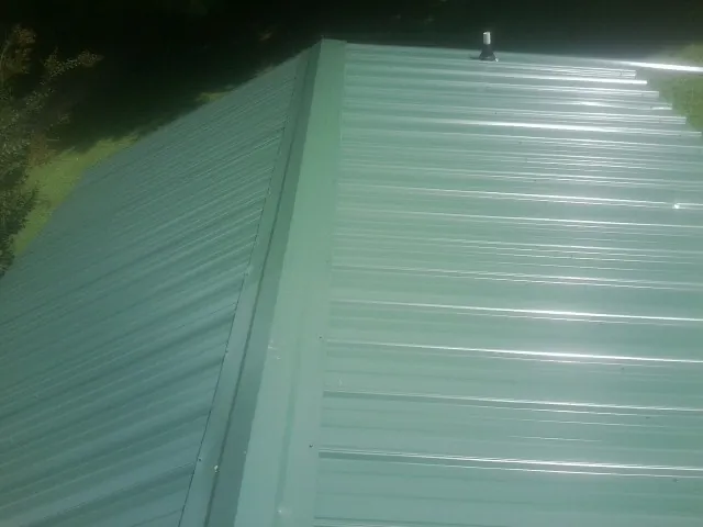 New green metal panels meeting at the ridge of a roof — Flat Roof Repair work by our crew in Toughkenamon