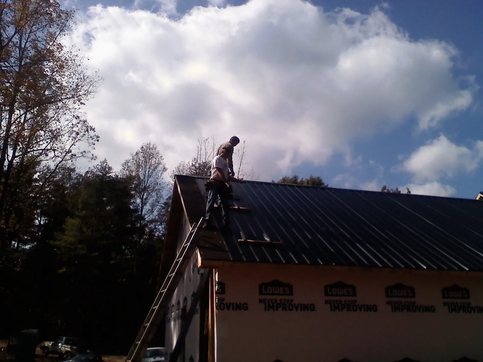Roofer fastening dark metal panels high against a cloudy sky, from a Roof Inspection job in Toughkenamon
