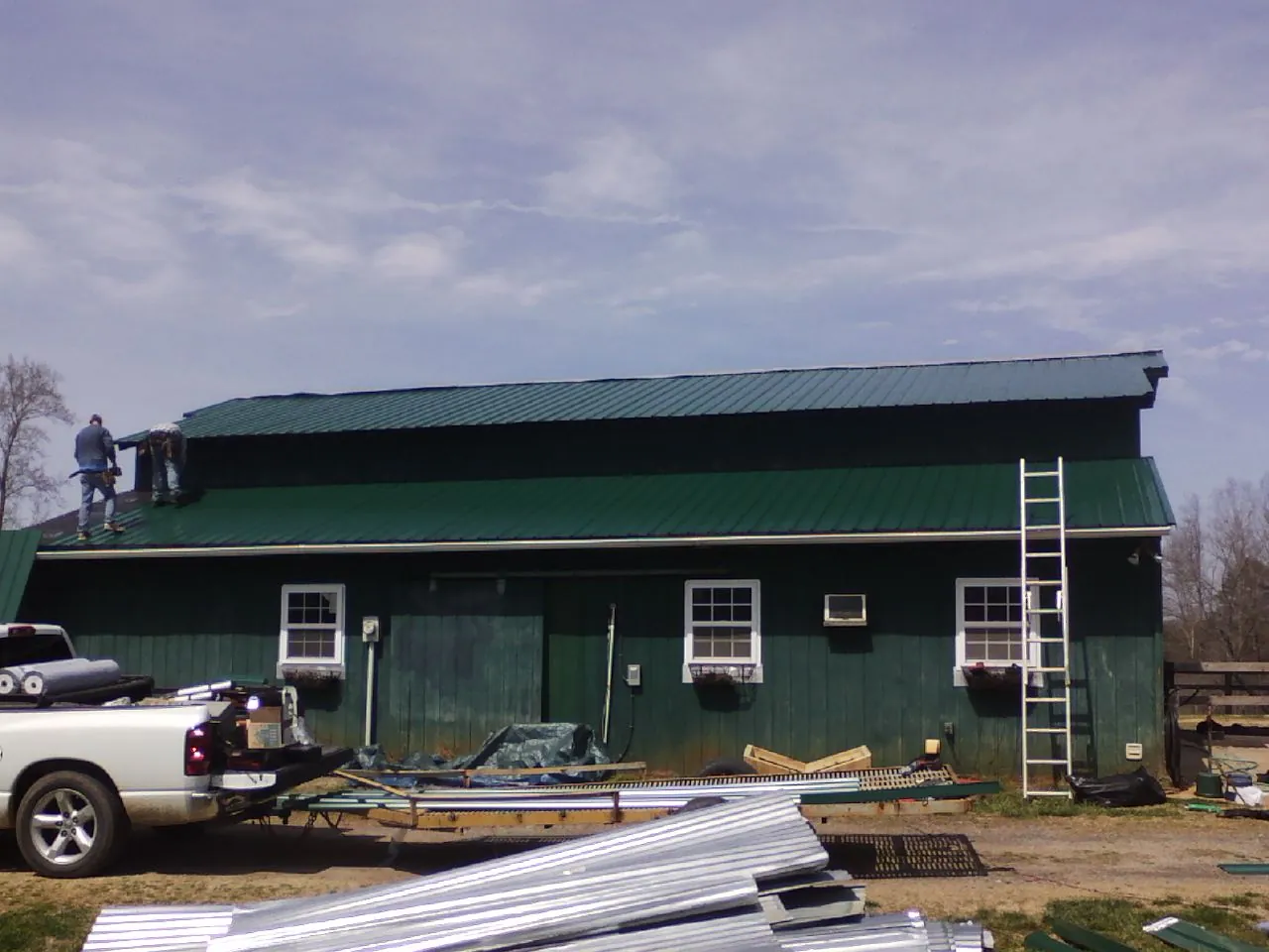 Crew installing green metal roofing on a large green barn in Toughkenamon
