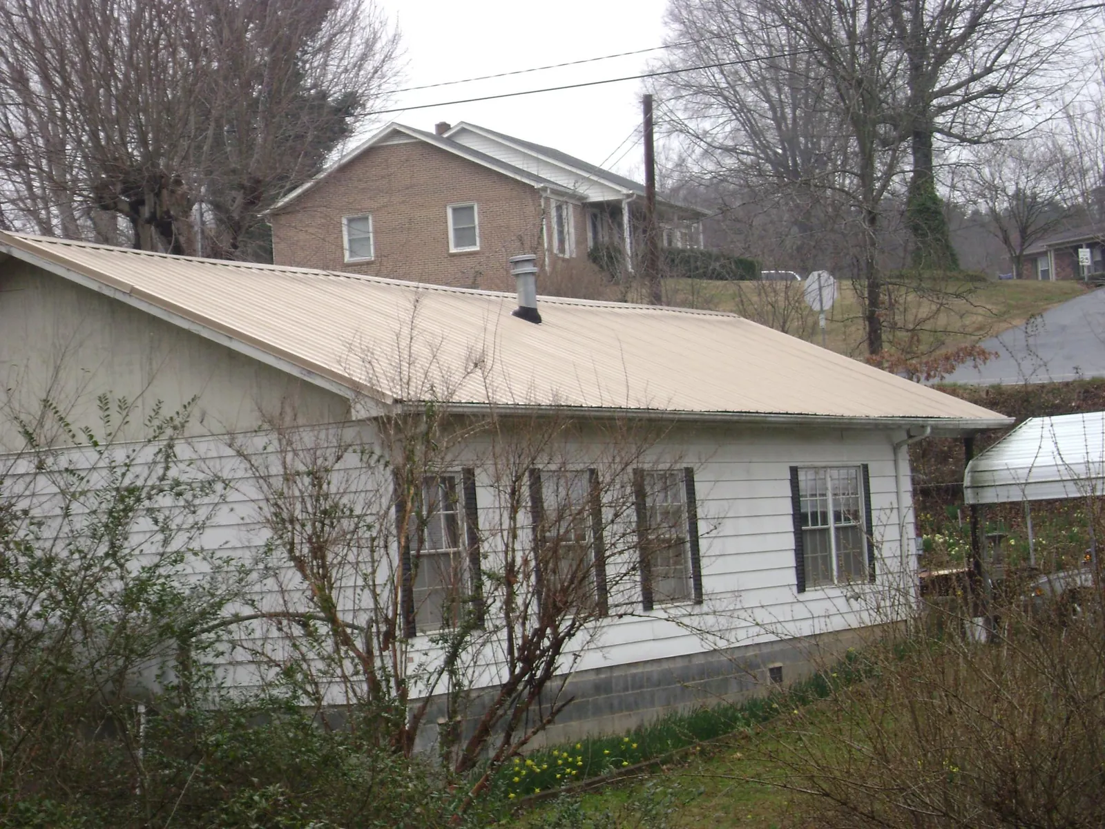 Tan metal roof on a white sided house set into a hillside — Commercial Roofing by Roofing Brothers in Toughkenamon